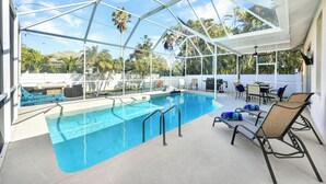 A covered outdoor swimming pool with lounge chairs and a table, surrounded by palm trees and a clear sky. - New! Sunkissed - 1 Mile to Beach! Heated Pool! (Naples)