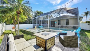 A covered outdoor patio with a pool, wicker furniture, and a palm tree. - New! Sunkissed - 1 Mile to Beach! Heated Pool! (Naples)