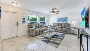 A living room with beige sofas, a coffee table, a ceiling fan, and a TV on the wall. - New Listing! Starfish Cove - Heated Pool, Walk to the Beach! (Naples)