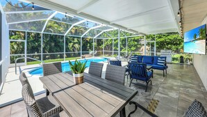 A covered outdoor area with a pool, wicker furniture, and a potted plant. - New Listing! Starfish Cove - Heated Pool, Walk to the Beach! (Naples)