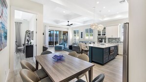 Een moderne keuken met een centraal kookeiland, inbouwapparatuur en een eethoek met een houten tafel en stoelen.