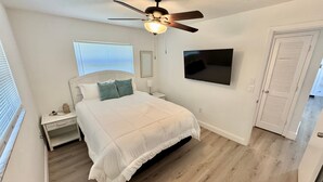 Une chambre à coucher avec un lit, un ventilateur de plafond, une télévision et une porte.