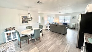 Uma cozinha moderna com geladeira, sala de jantar com mesa e cadeiras, e sala de estar com sofá e mesa de centro.