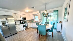 Cozinha moderna com eletrodomésticos de aço inoxidável, sala de jantar com cadeiras cor turquesa e uma janela grande com cortinas.