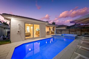 A residential swimming pool with a covered patio area and a house with a sliding glass door.