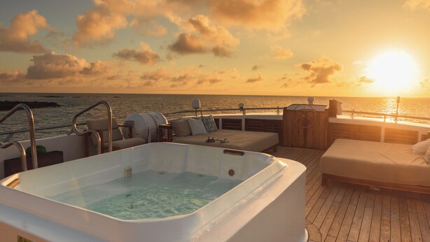 Ein Whirlpool auf einer Holzterrasse mit Blick auf das Meer bei Sonnenuntergang.
