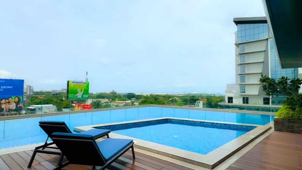 A rooftop swimming pool with lounge chairs, surrounded by a wooden deck and a modern building. - Bella Suite Bacolod (Bacolod)
