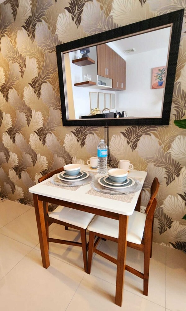 Un área de comedor con una mesa lista para dos personas, una botella de agua y un televisor montado en la pared.