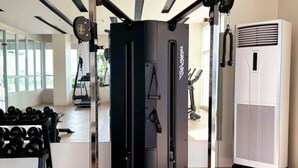 A gym with a weight machine, dumbbells, and a large air conditioner. - Bella Suite Bacolod (Bacolod)