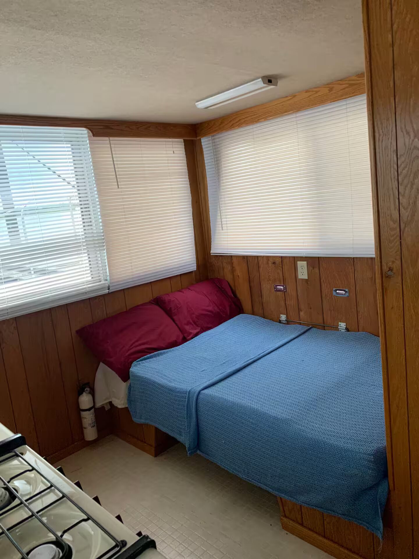 A compact RV bedroom with a bunk bed, wooden walls, and a small kitchenette.