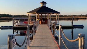 A pier leading to a covered dock with a small pavilion, boats docked, and a calm water body in the background. - Maggie Jo’s paradise on the river ! (Georgetown)