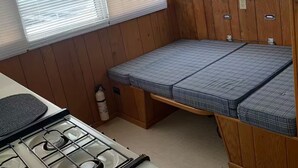 A compact RV kitchen with a stove, a small sink, and a bed with a blue mattress. - Maggie Jo’s paradise on the river ! (Georgetown)