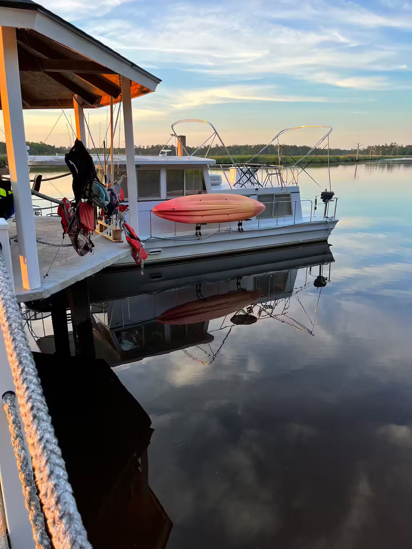 A boat docked at a calm lake with a covered area and kayaks.