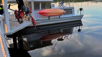 A boat docked at a calm lake with a covered area and kayaks.