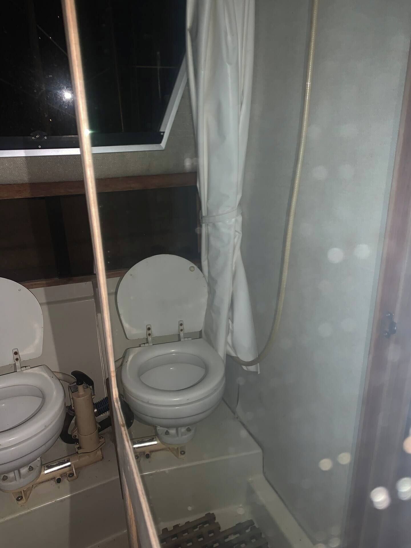 Een kleine badkamer met twee toiletten, een douchegedeelte en een raam.