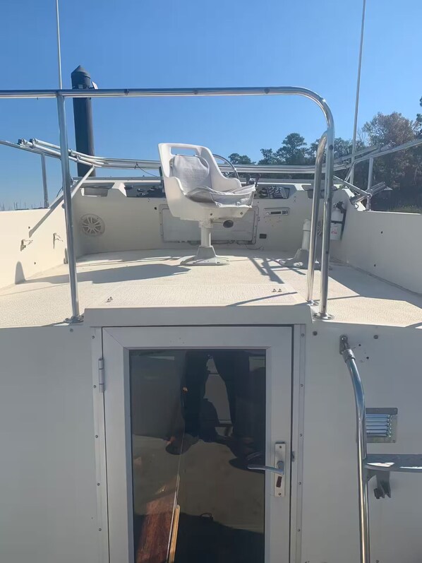 A boat deck with a white cushioned seat, metal railings, and a door leading to the interior.
