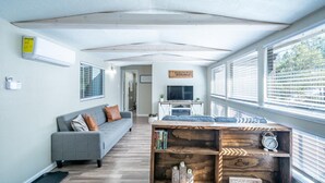 A modern living room with a grey sofa, a wooden bookshelf, and a television. - Serenity Hideaway, Charming 2bd/1ba cabin with WiFi, AC, close to shops (Ruidoso)
