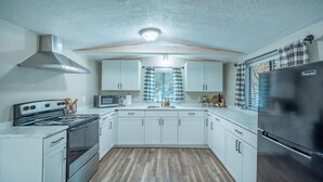 A compact kitchen with white cabinets, a stove, microwave, and a refrigerator. - Serenity Hideaway, Charming 2bd/1ba cabin with WiFi, AC, close to shops (Ruidoso)