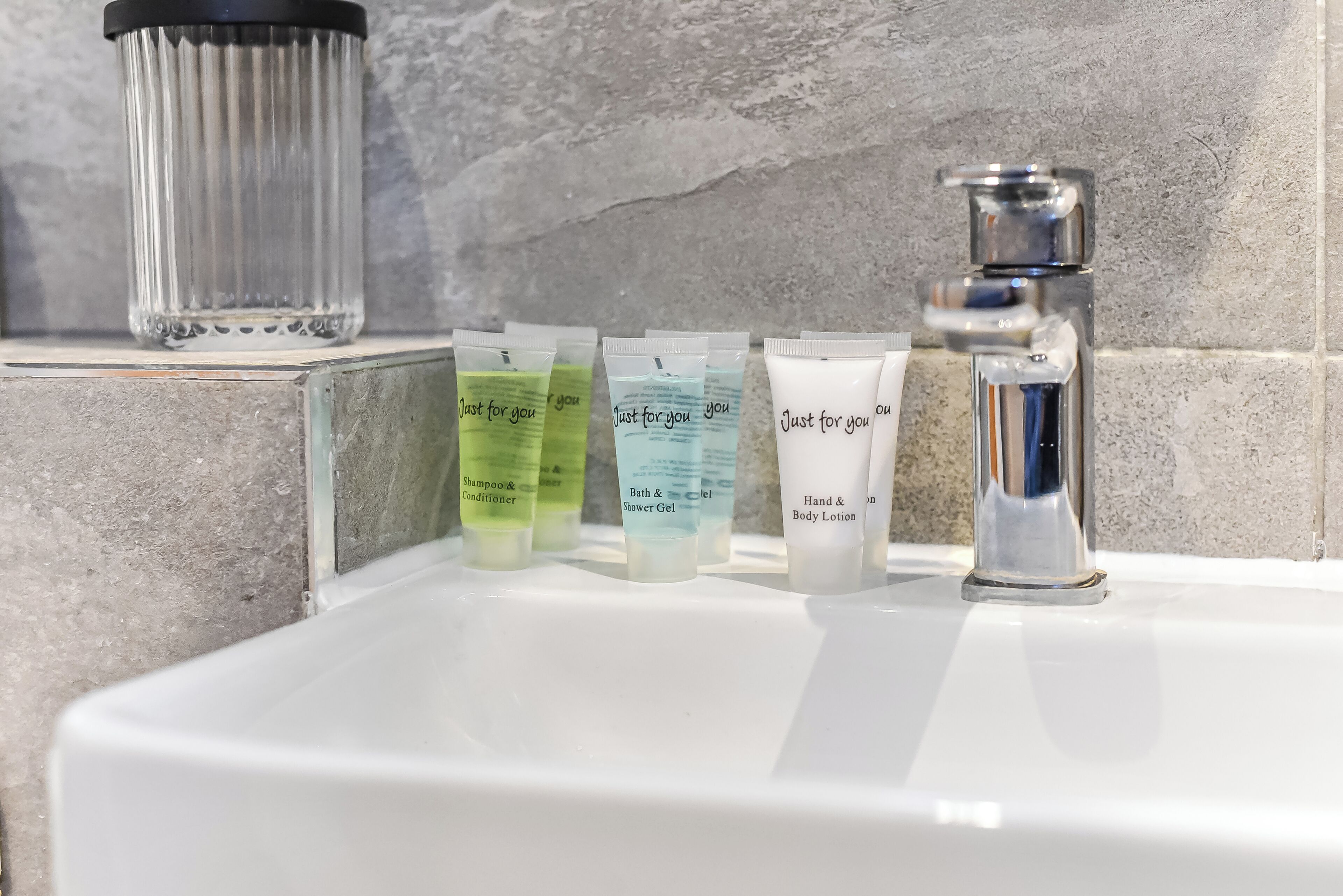 Un lavamanos de baño con distintos artículos de aseo, como champú, acondicionador, gel de ducha y loción corporal.