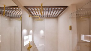 Ein modernes Badezimmer mit einer Duschkabine aus Glas, einem goldfarbenen Duschkopf und einer Decke mit geometrischem Muster.