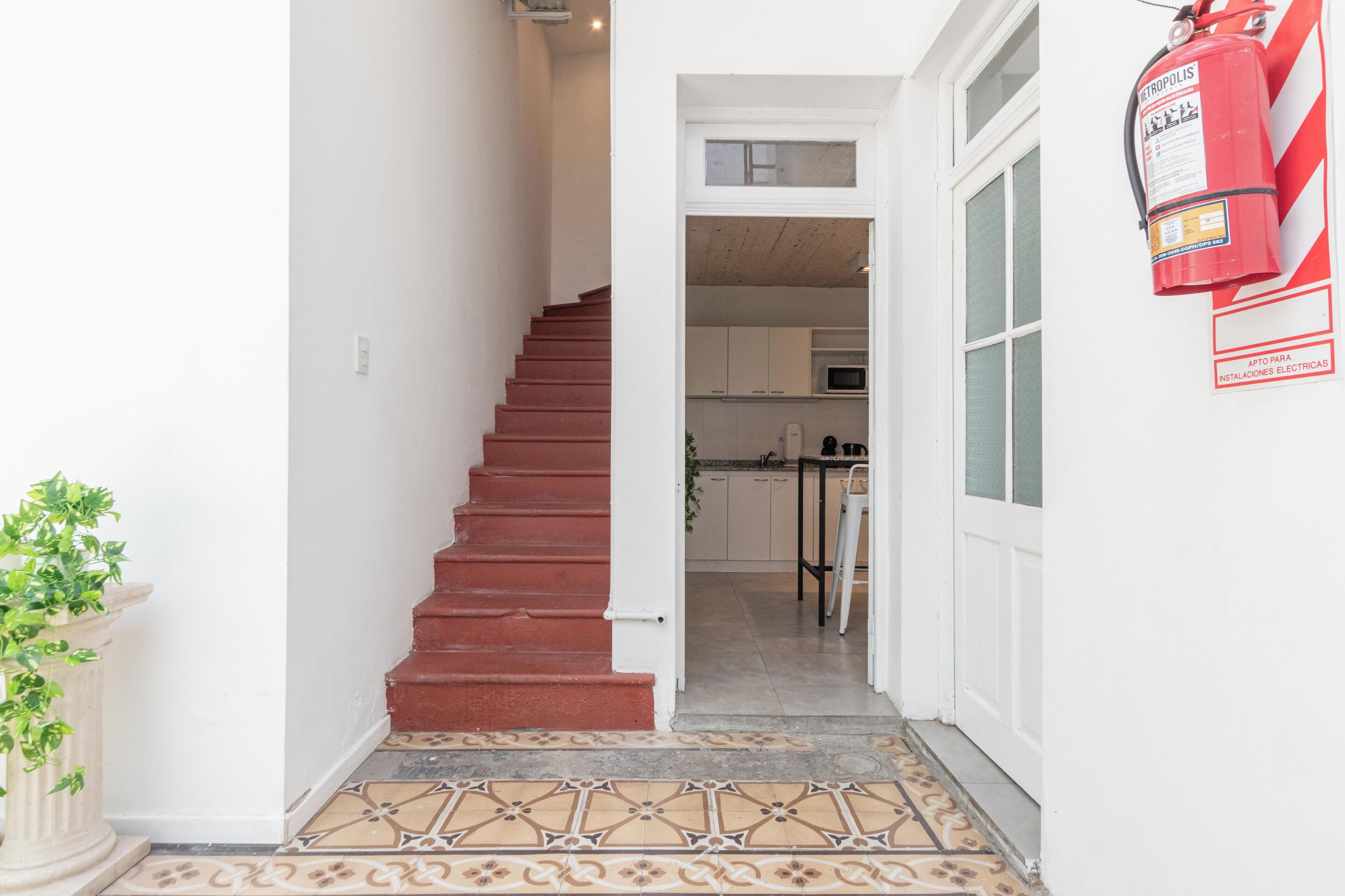 Una escalera conduce a una cocina con armarios blancos y un extintor rojo montado en la pared.