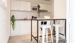 Een moderne keuken met witte kastjes, een granieten aanrecht, een magnetron, een koffieapparaat en twee witte barkrukken.