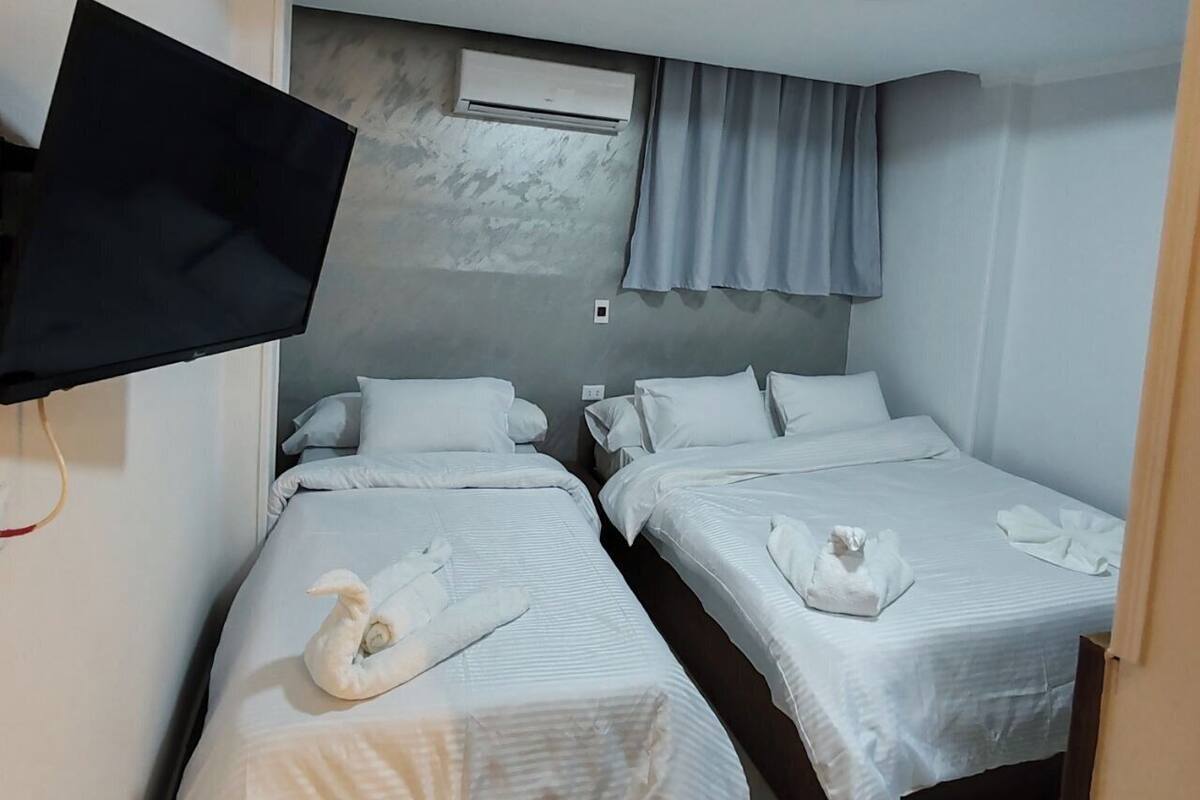 A hotel room with two beds, a flat-screen TV mounted on the wall, and a ceiling light.