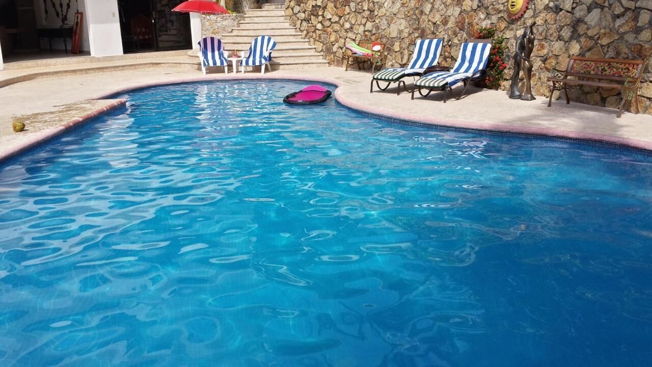 Una piscina con agua azul, rodeada de sillas de descanso y un muro de piedra.