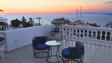 Terraza con dos sillas y una mesa, con vista a un cuerpo de agua al atardecer.