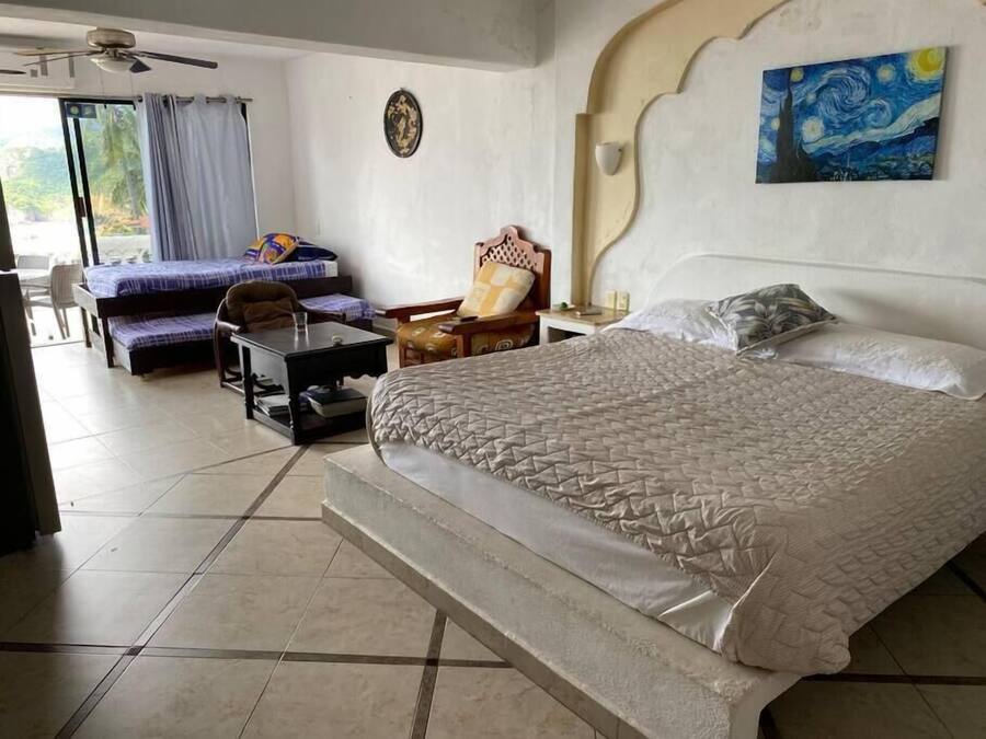 Una habitación de hotel con una cama grande, una silla, una mesita y un cuadro en la pared.