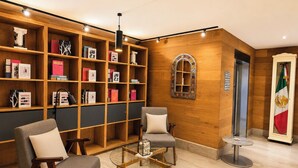Un hall de hotel con una estantería de madera, dos sillones, una mesa de centro de vidrio y una bandera.