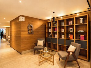 A hotel lobby with a wooden reception desk, two armchairs, a glass coffee table, and a bookshelf filled with books. - Cerca de ti Residencia  (Mexico City)
