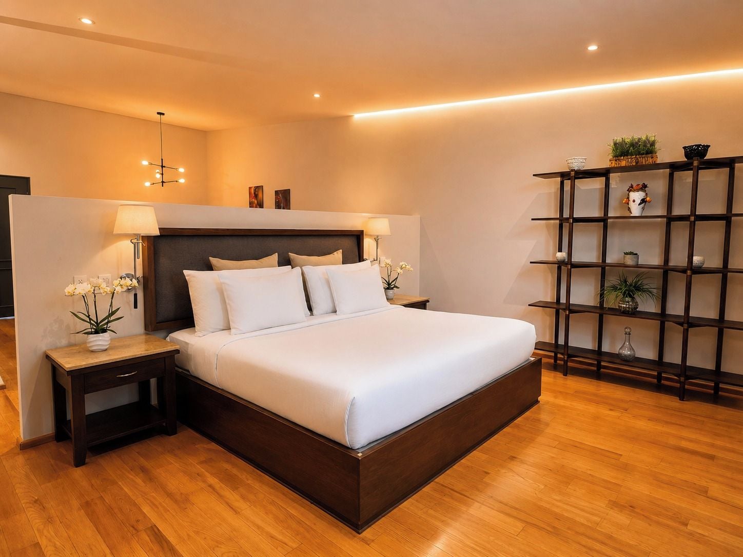 Una habitación de hotel moderna con una cama grande, lámparas de noche, suelo de madera y una estantería empotrada.