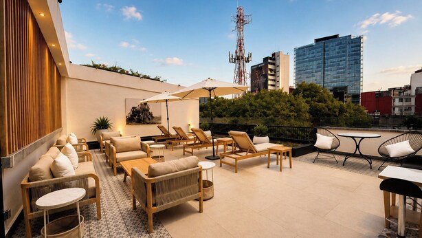 Un área de lounge en la azotea con mobiliario exterior, incluyendo sofás y sillones, y vistas de la ciudad al fondo.