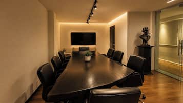 A conference room with a long table, black chairs, a potted plant, and a mounted flat-screen TV.