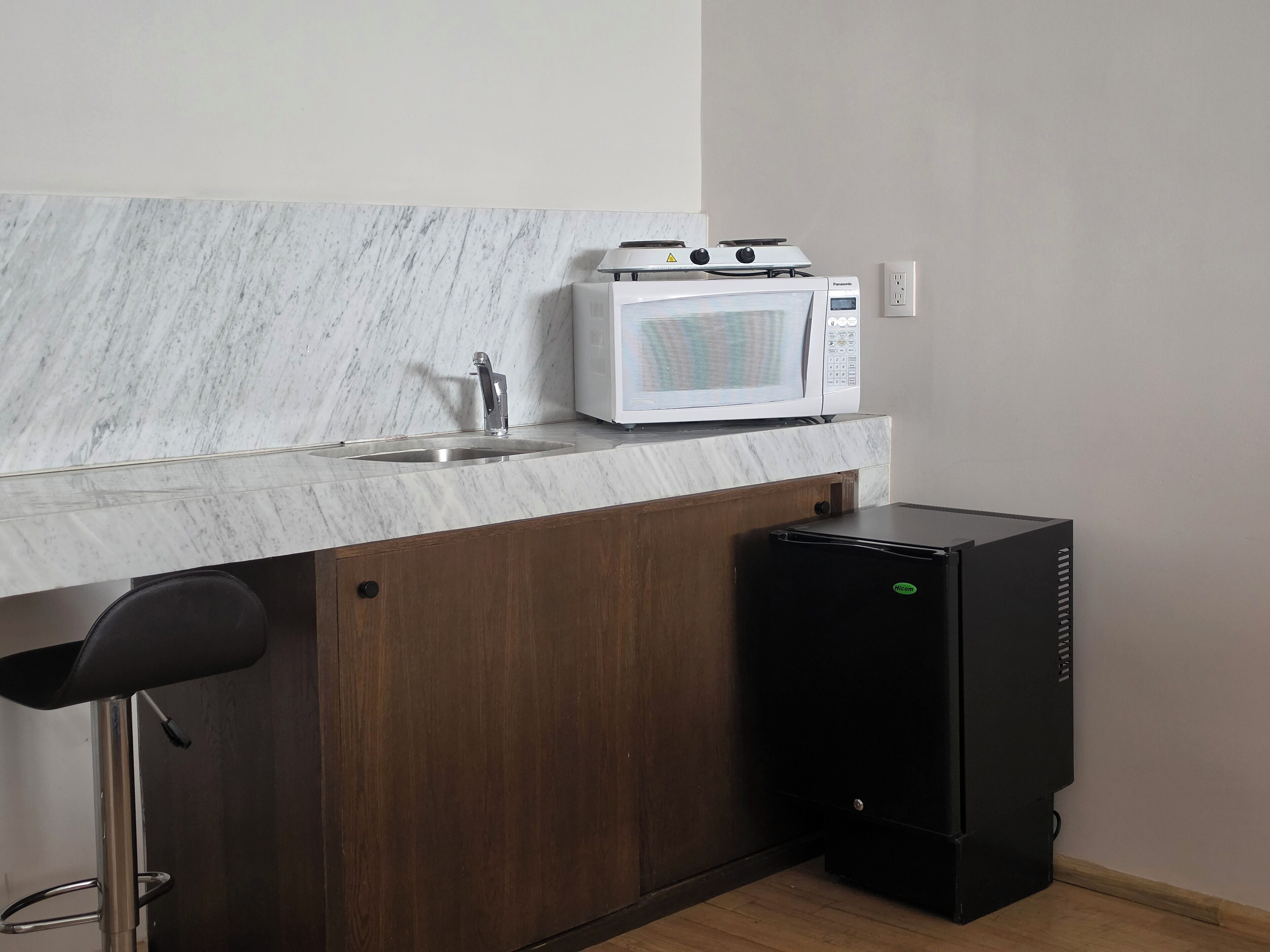 Una cocina compacta con un lavamanos, un microondas blanco y un refrigerador negro.