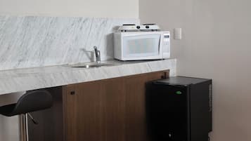 Una cocina compacta con un lavamanos, un microondas blanco y un refrigerador negro.