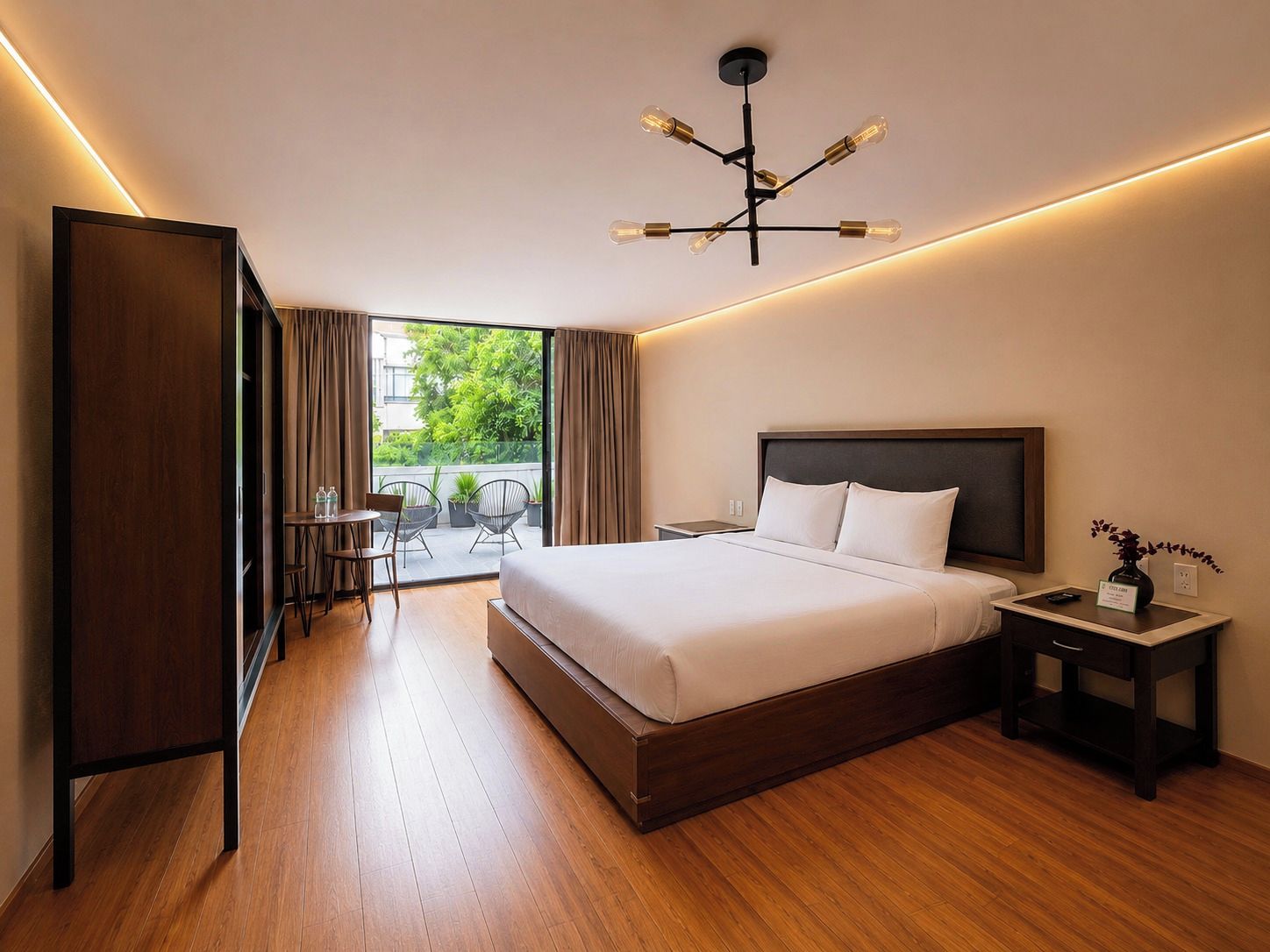 Una habitación de hotel con una cama grande, una mesita de noche, una silla, una pequeña mesa con sillas y vistas al exterior.