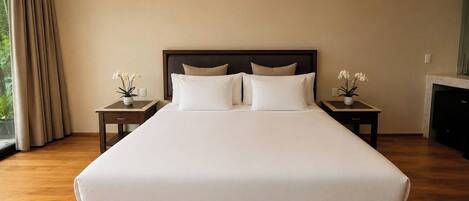 A large bed with a wooden frame, two bedside tables with lamps, and a view of greenery outside.