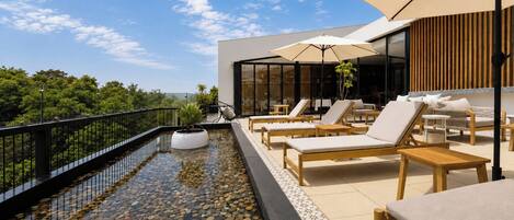 Terraza en la azotea con piscina, sillones y sombrillas.