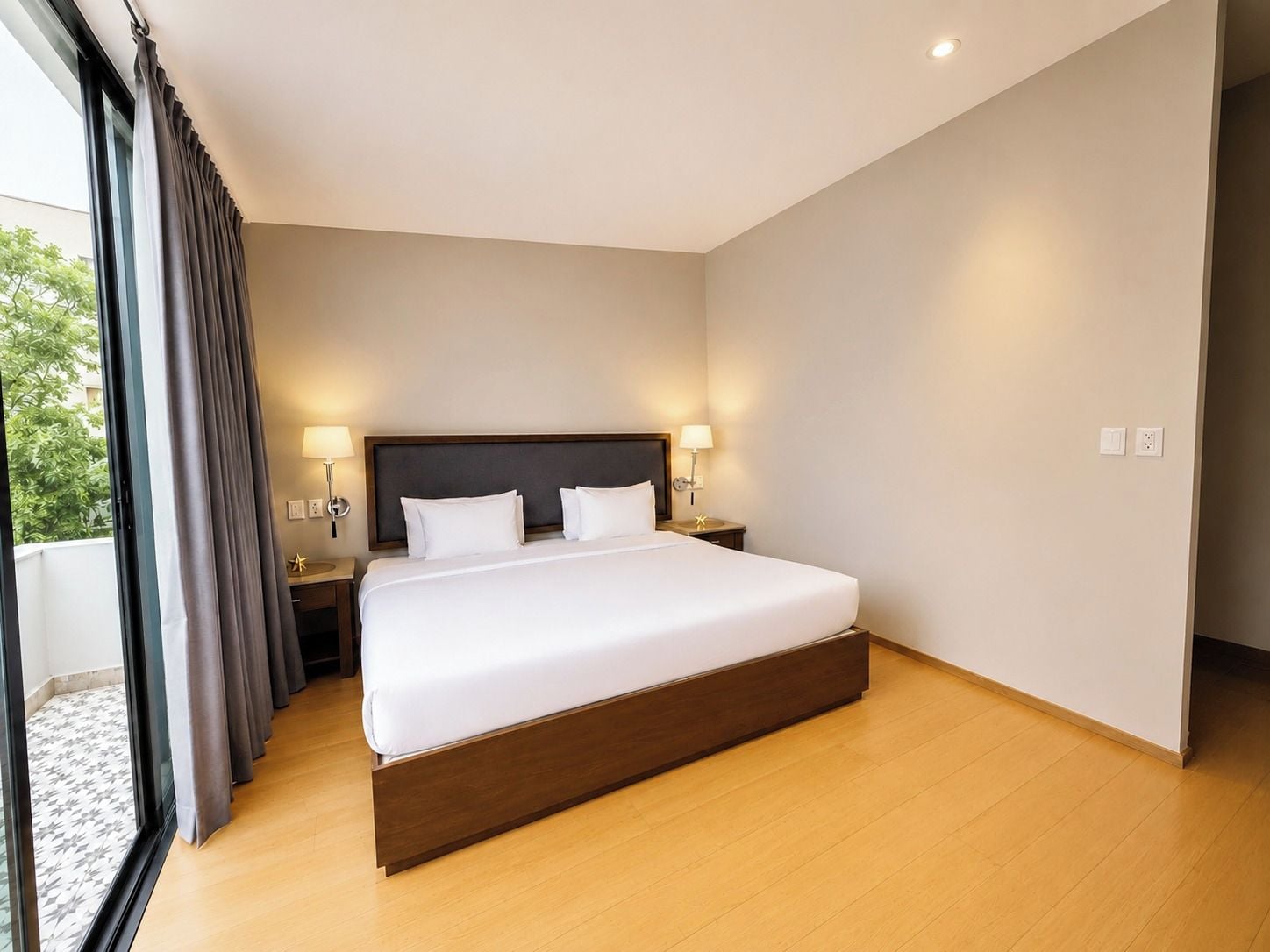 Ein modernes Hotelzimmer mit einem großen Bett, zwei Nachttischlampen und Blick durch ein Fenster mit Vorhängen.