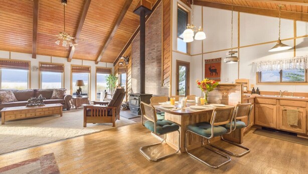 A spacious living area with a high ceiling, wooden beams, a fireplace, and a dining area with a table and chairs.