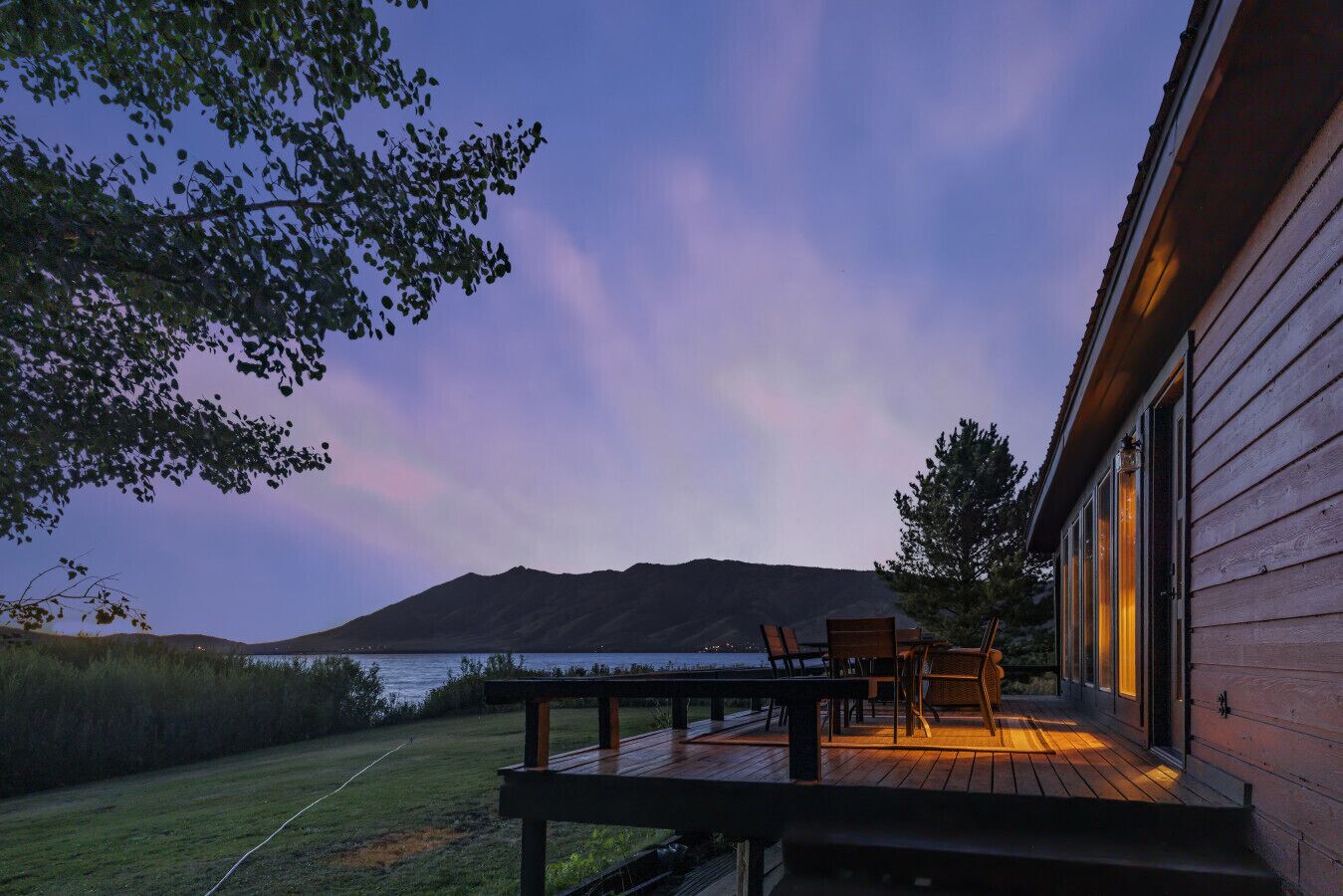 A wooden deck with outdoor furniture, overlooking a body of water and a mountain range.
