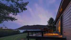A wooden deck with outdoor furniture, overlooking a body of water and a mountain range.