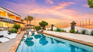 A swimming pool with lounge chairs, a building with balconies, and a sunset sky. - Beachfront Condo | Pool + Hot Tub | View (Galveston)