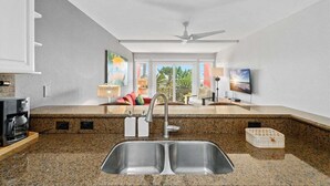 A kitchen with granite countertops, a double sink, a coffee maker, and a ceiling fan. - Beachfront Condo | Pool + Hot Tub | View (Galveston)