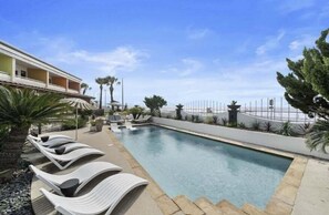Una piscina con sillas de descanso, una palmera y un edificio al fondo.
