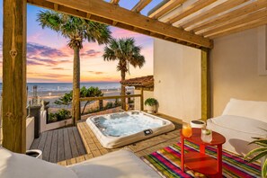 Une terrasse en bois avec un jacuzzi, une chaise longue et une table avec des boissons.