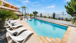 Une piscine avec des chaises longues, une clôture blanche et des palmiers.