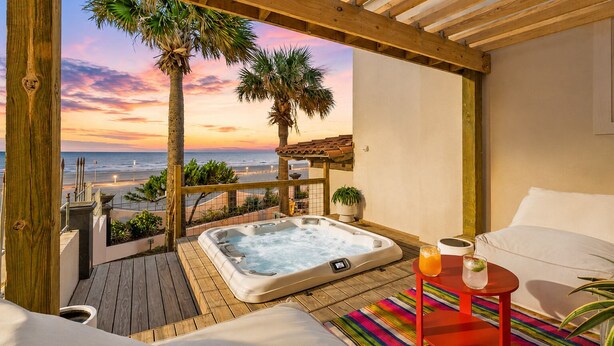 Une terrasse en bois avec un jacuzzi, une chaise longue et une table avec des boissons.
